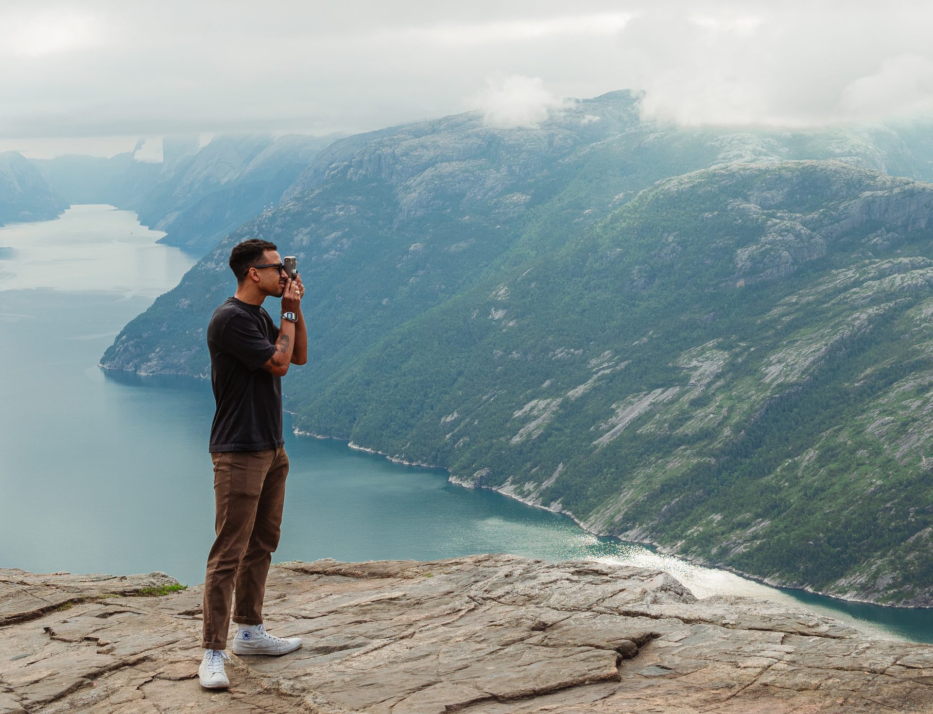Cameron shooting with a film camera on a cliff edge above a Norwegian fjord